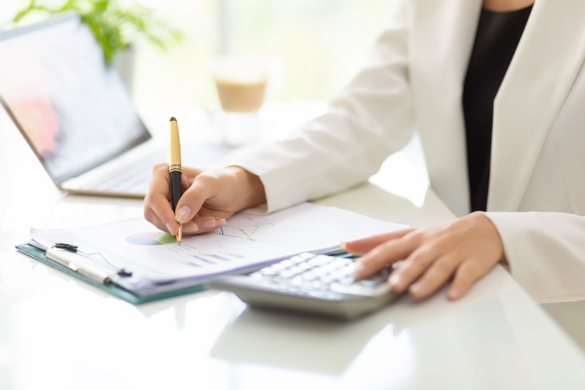 A close-up of hands of a financial advisor working with a document, a laptop, and a calculator on a table.