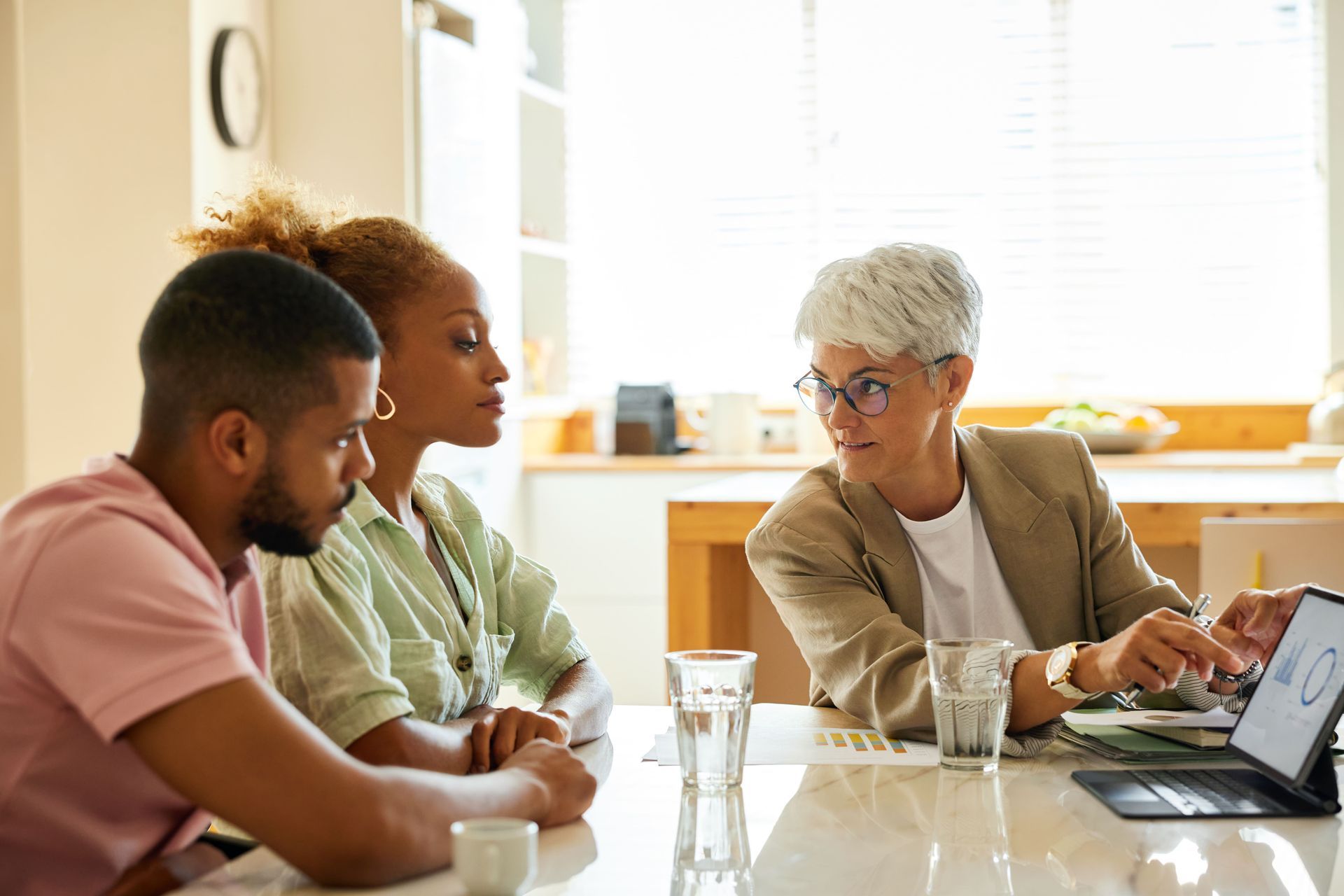 A smiling financial advisor discussing finances with a young couple sitting at table.