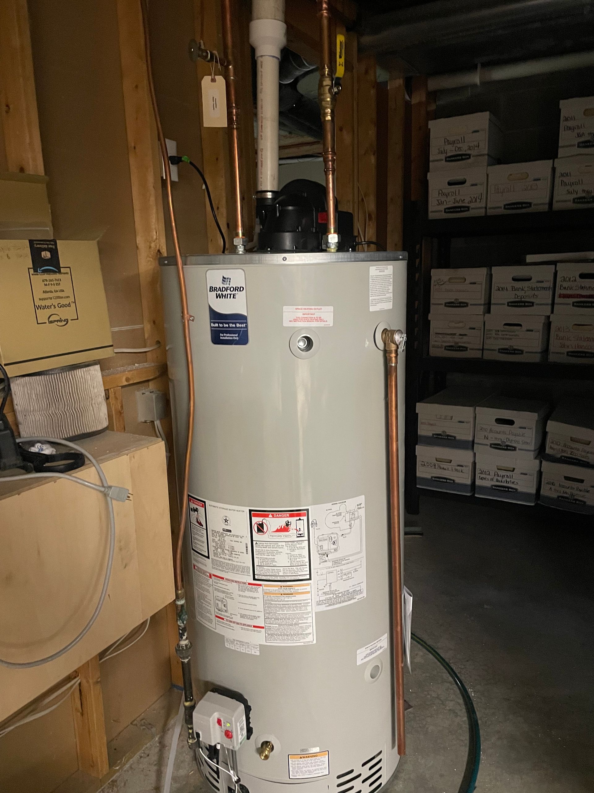 A water heater is sitting in a garage next to boxes.