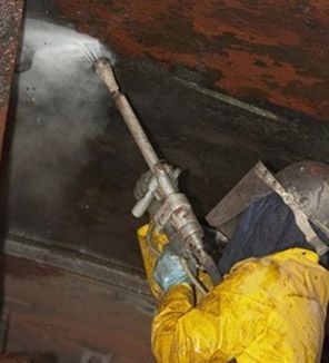Trabajador con equipo de protección amarillo usando una pistola de agua a alta presión. El chorro crea niebla.