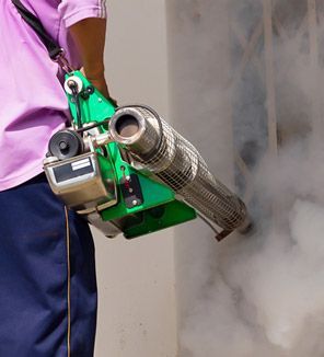 Persona que utiliza un nebulizador verde que emite humo blanco, al lado de una pared.