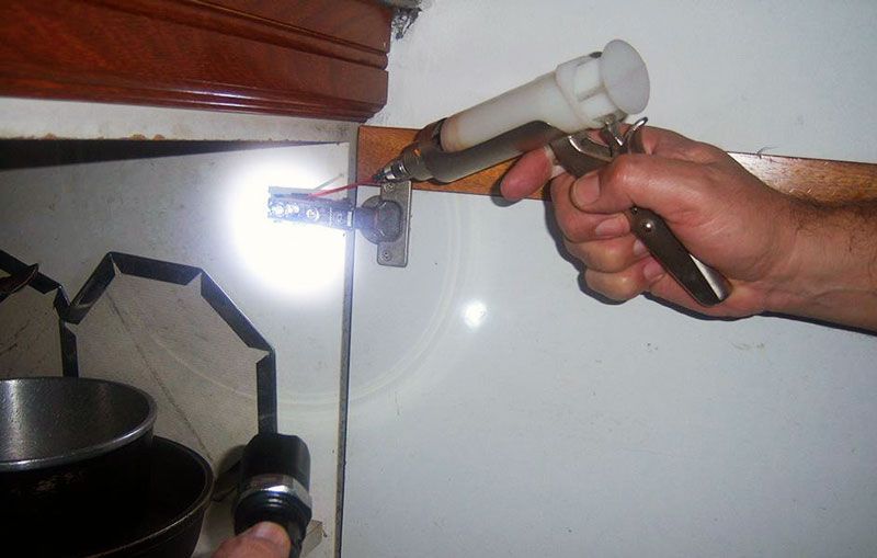 Persona que utiliza alicates en un artefacto de plomería debajo de un gabinete, iluminado por una linterna.