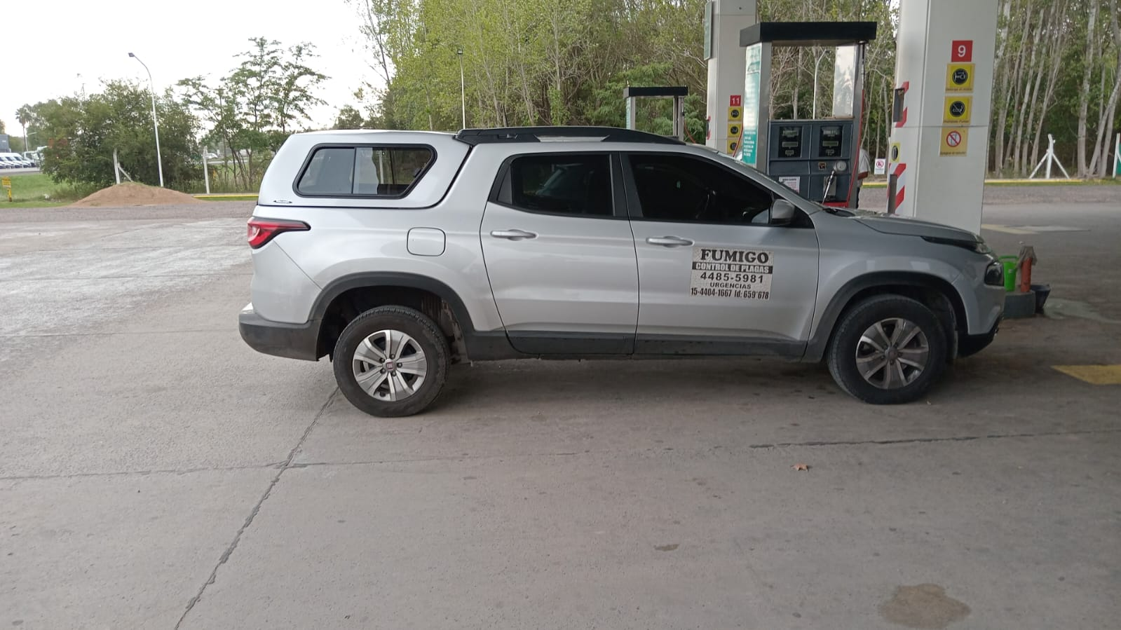 Camioneta plateada en una gasolinera, con capota en la caja, estacionada en un surtidor.