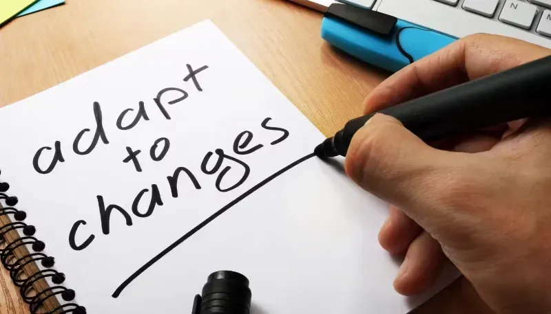 A person is writing in a notebook that says adapt to changes