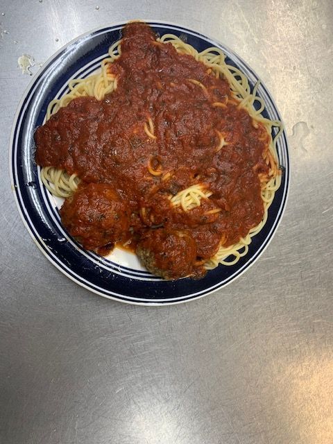 A plate of spaghetti topped with a rich red tomato sauce and two large meatballs on a stainless steel surface.