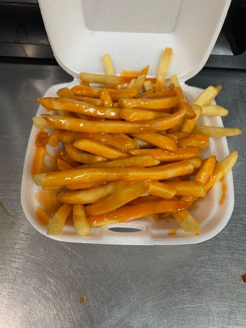 A styrofoam container filled with golden-brown french fries drizzled with melted orange cheese on a stainless surface.