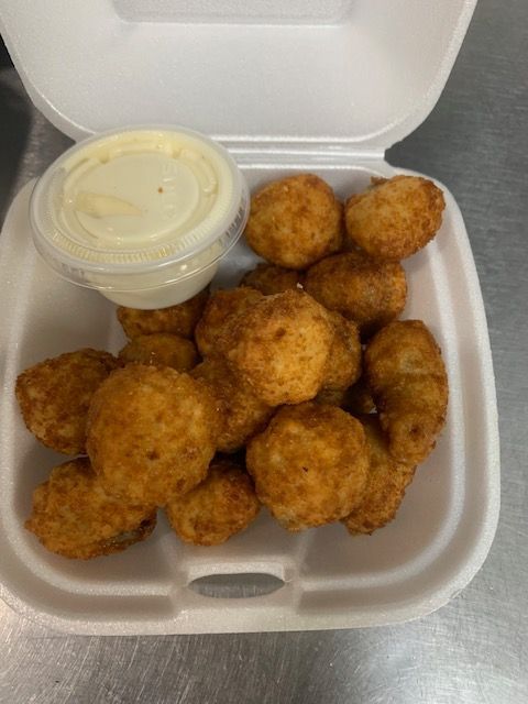A white styrofoam takeout container filled with fried cheese curds and a side of creamy white dipping sauce.