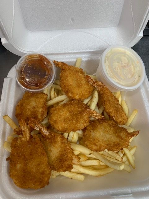 A takeout container filled with breaded fried shrimp and french fries, accompanied by a side of cocktail and tartar sauce.