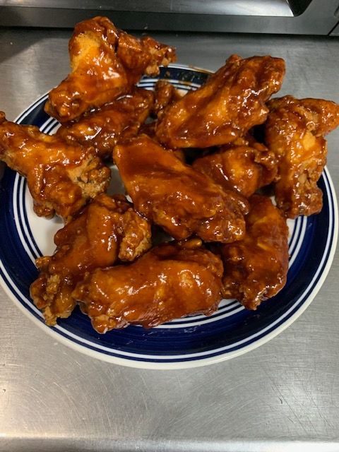 A plate of chicken wings coated in a glossy, reddish-brown barbecue sauce sitting on a stainless steel surface.
