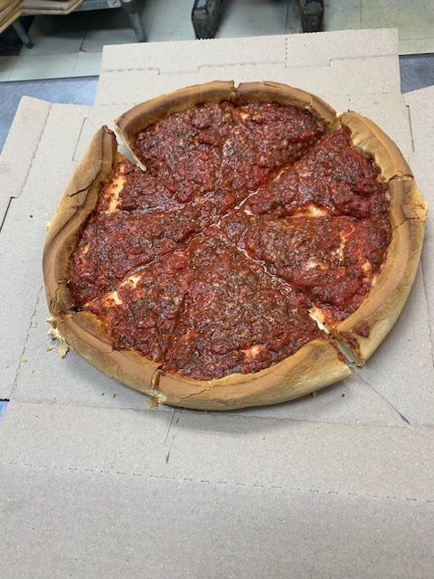 A deep-dish pizza with thick, golden-brown crust and red tomato sauce, sliced and presented in a cardboard pizza box.
