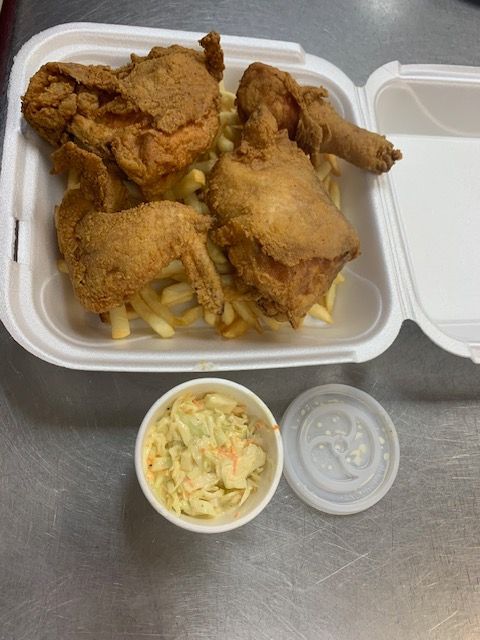 A meal of fried chicken and french fries in a white to-go container next to a small cup of coleslaw on a metal table.