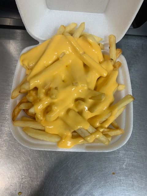 A styrofoam takeout container filled with golden-brown french fries generously topped with melted yellow cheese sauce.
