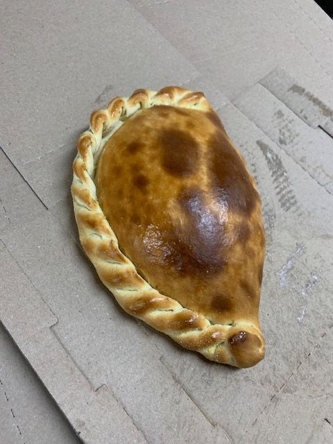 A golden-brown baked empanada with a braided crust edge, resting on a flat, light-colored cardboard surface.