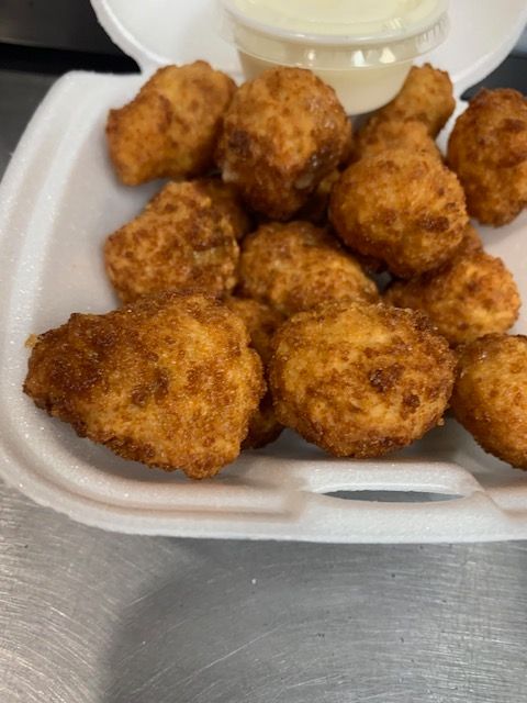 A container filled with golden-brown fried food bites and a small side of white dipping sauce.
