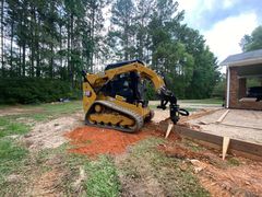 A bulldozer is digging a hole in the dirt in front of a house.