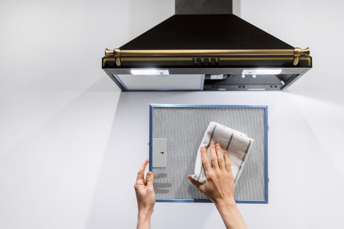 Chef cleaning commercial kitchen vent hood with sponge.