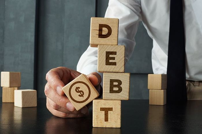 A man is stacking wooden blocks with the word debt on them.