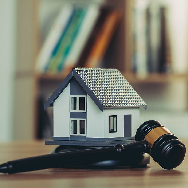 A small house is sitting on top of a wooden table next to a judge 's gavel.