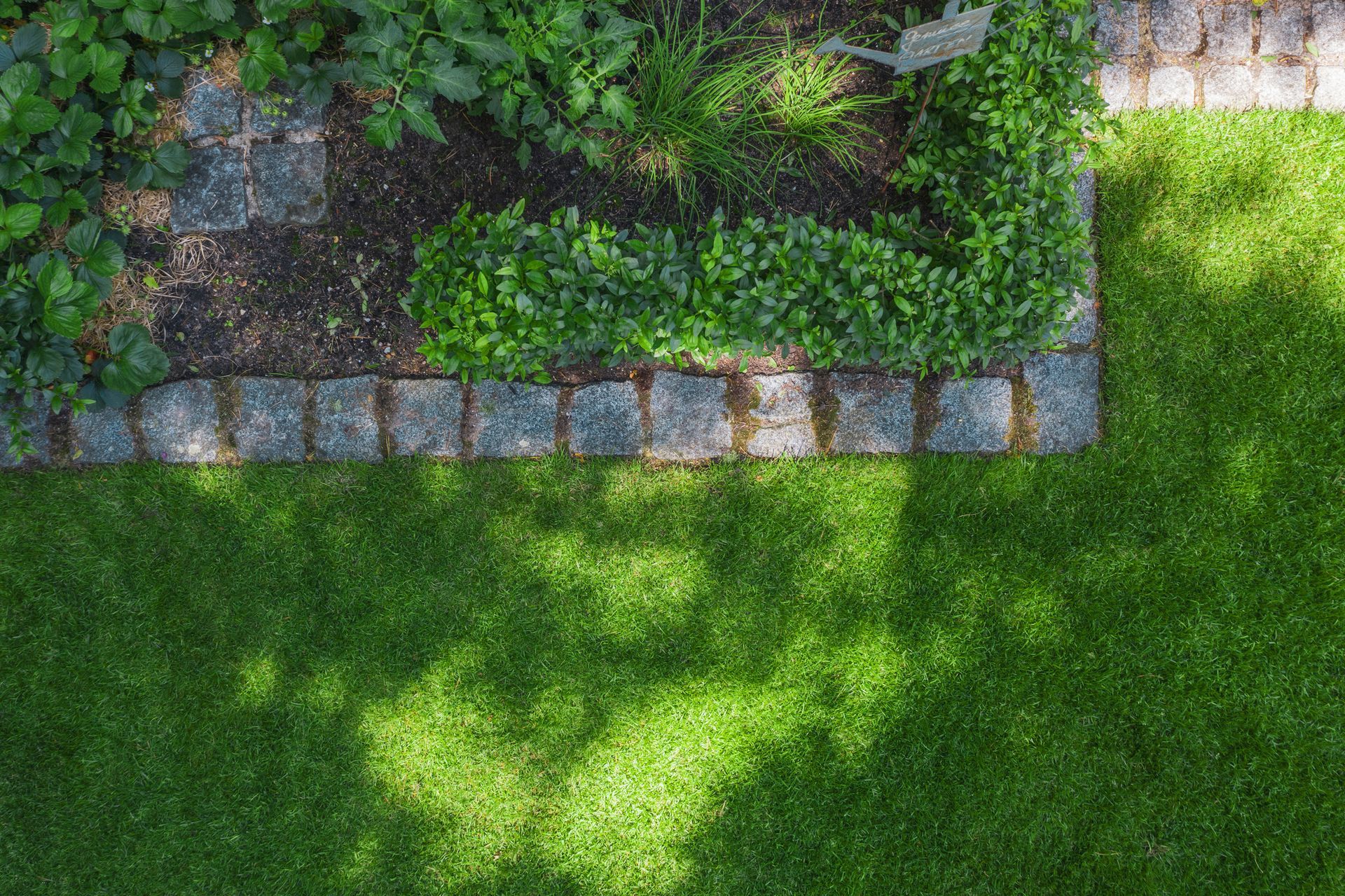 A garden bed bordered with stone edging next to a lush green lawn.