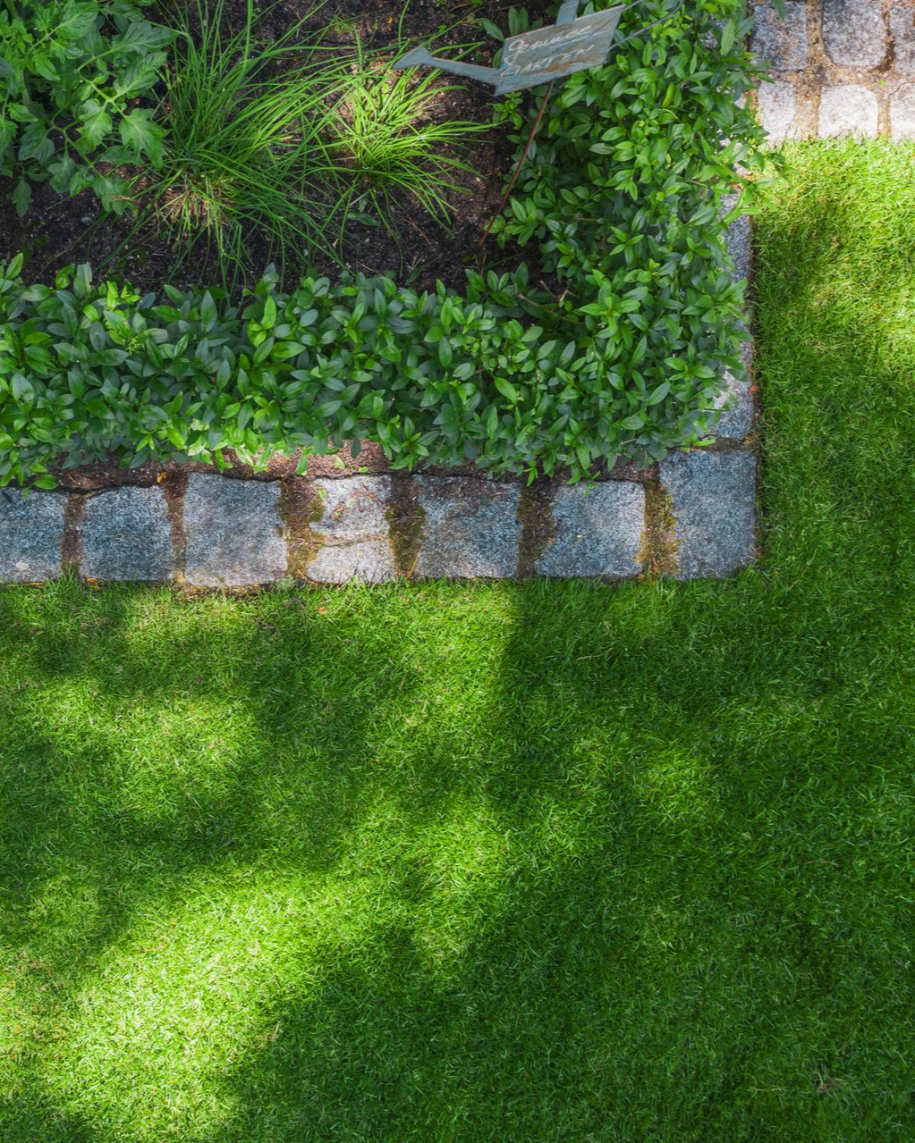 A garden bed bordered with stone edging next to a lush green lawn. A garden bed bordered with stone edging next to a lush green lawn.