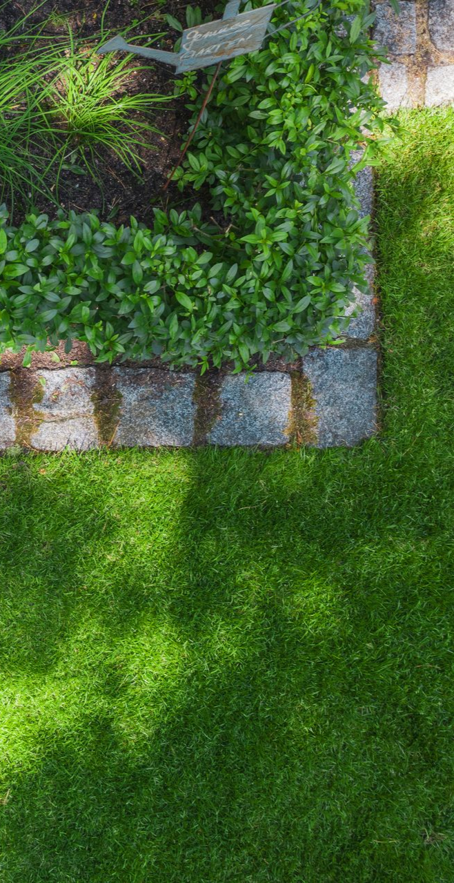 A garden bed bordered with stone edging next to a lush green lawn. A garden bed bordered with stone edging next to a lush green lawn.