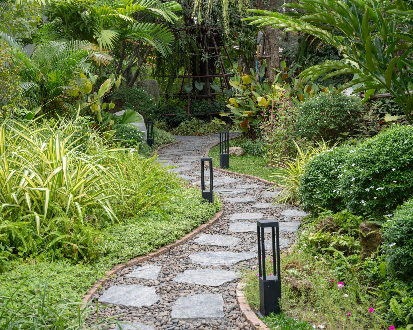 A winding stone pathway surrounded by lush green plants and garden lights. A winding stone pathway surrounded by lush green plants and garden lights.