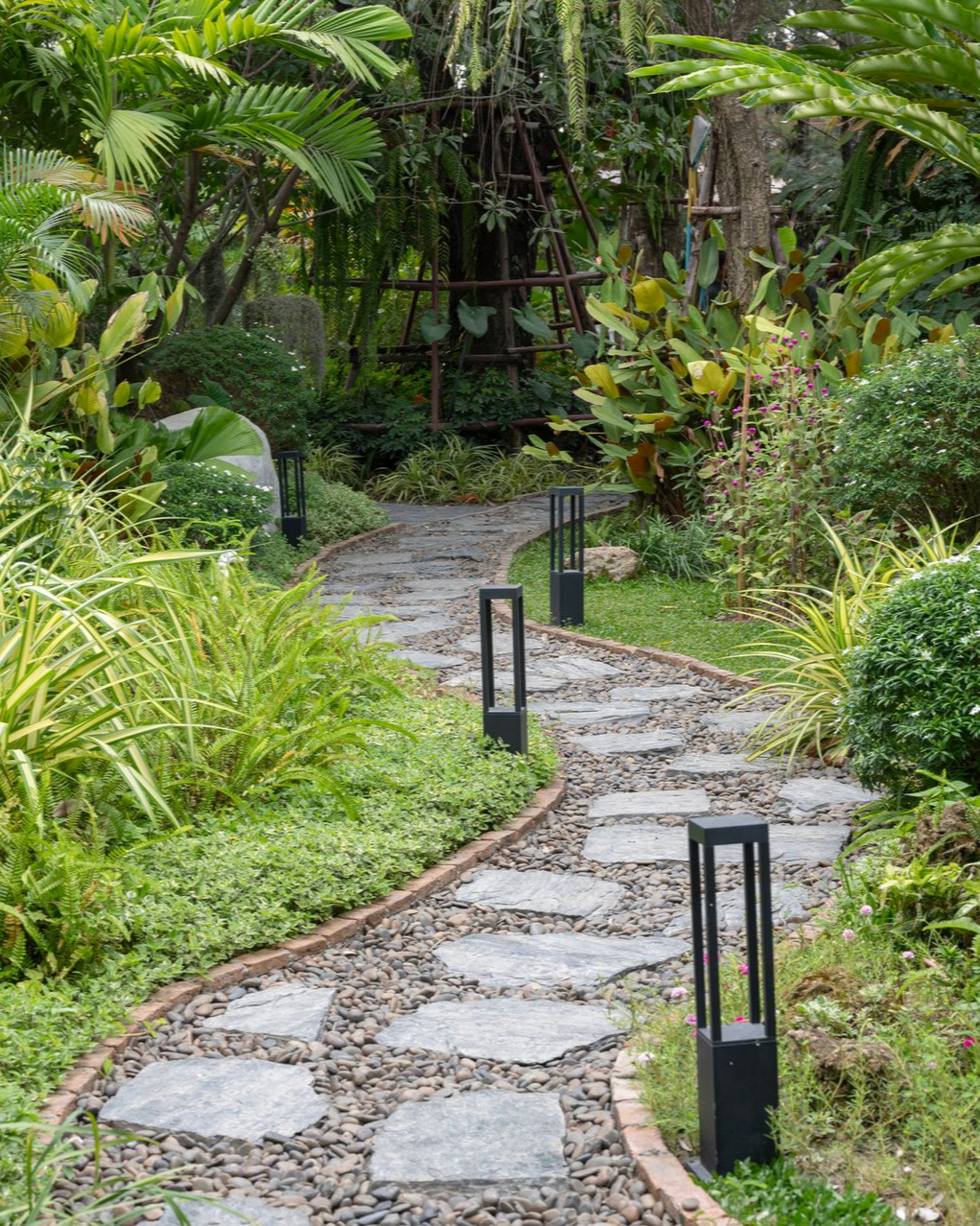 A winding stone pathway surrounded by lush green plants and garden lights. A winding stone pathway surrounded by lush green plants and garden lights.