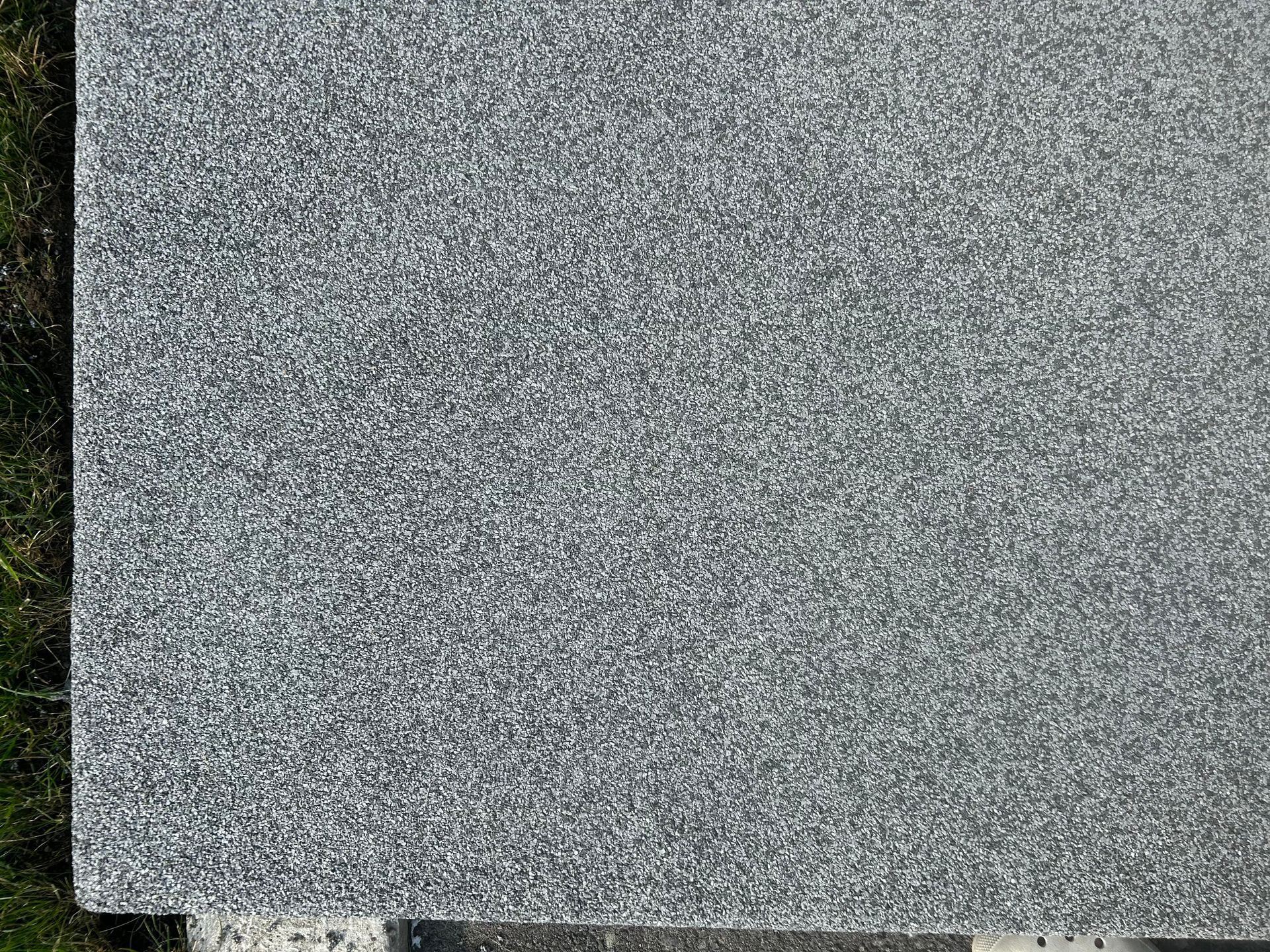 Un gros plan d'une tuile de granit gris posée sur un champ couvert d'herbe.