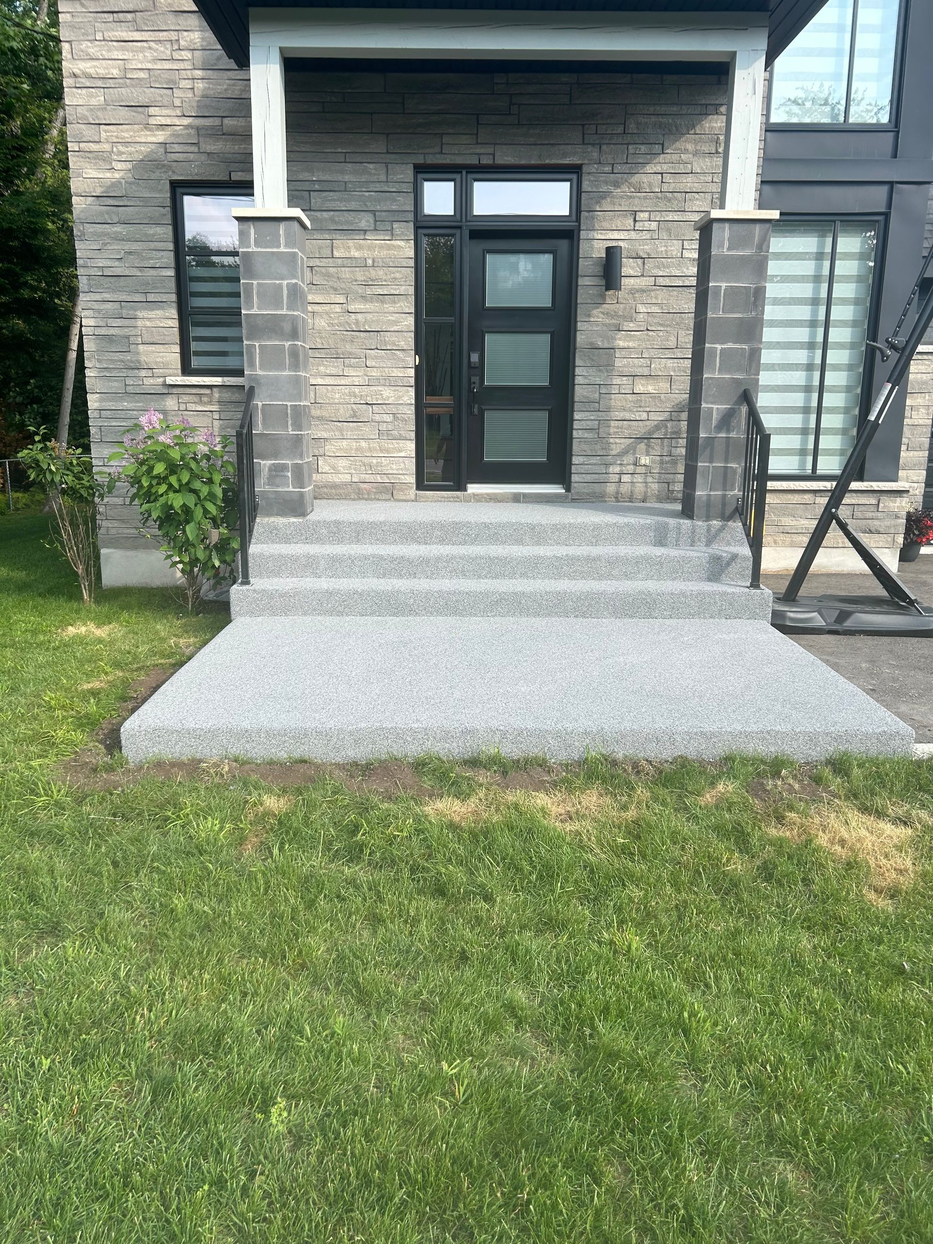 Un porche en béton avec des escaliers menant à la porte d'entrée d'une maison.