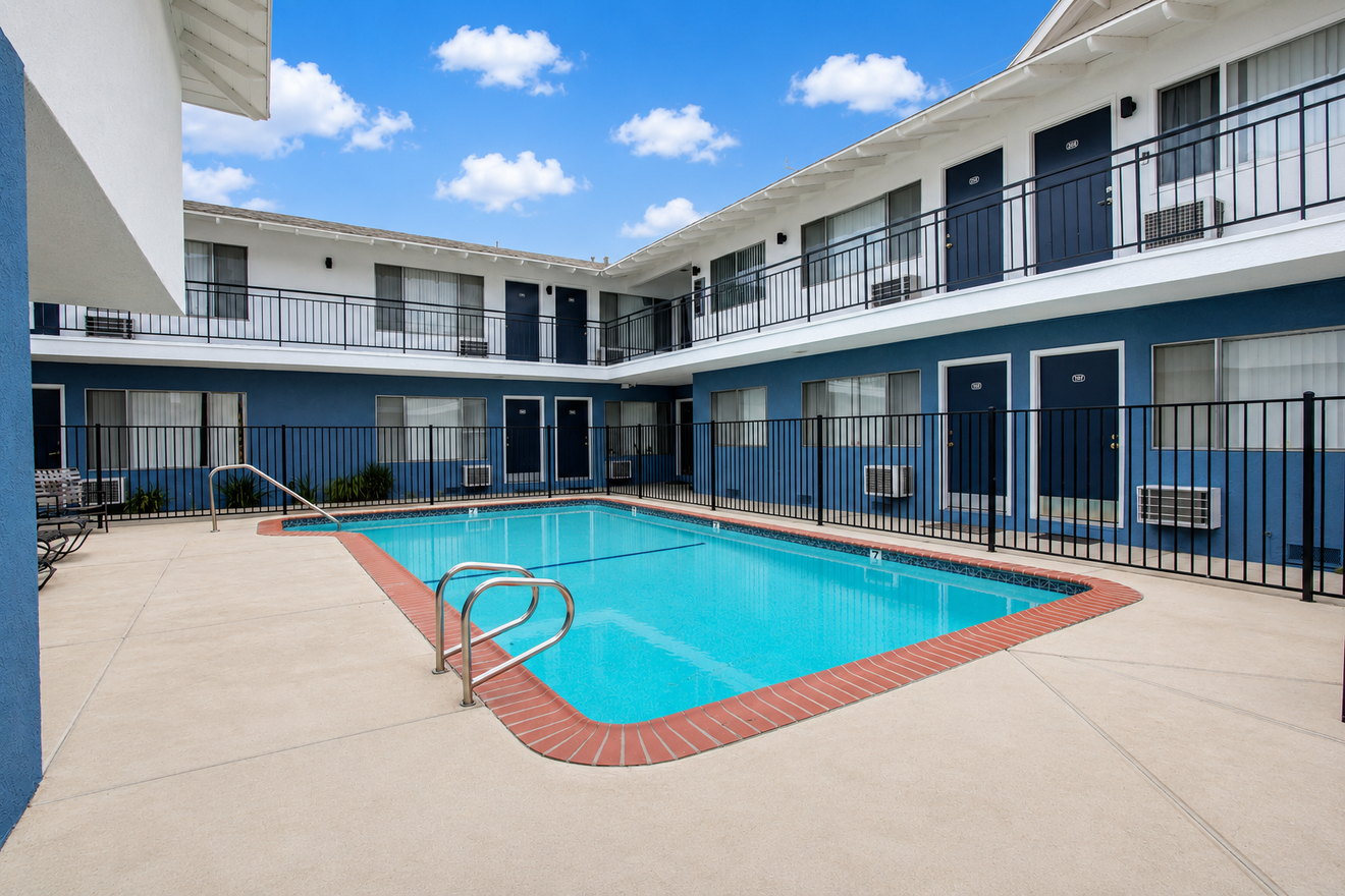 Courtyard motel pool with blue water, red brick border, and two-story rooms around it