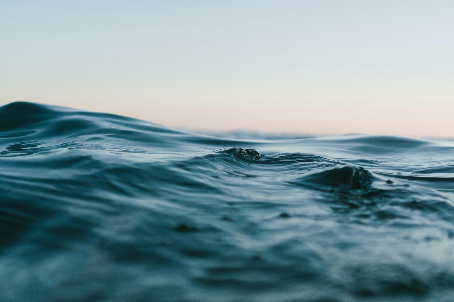 Ocean water close-up with small waves, light blue, and a clear sky in the distance.
