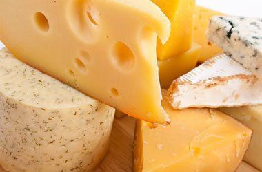 a variety of cheeses are on a wooden cutting board .