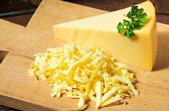 a slice of cheese and shredded cheese on a wooden cutting board .