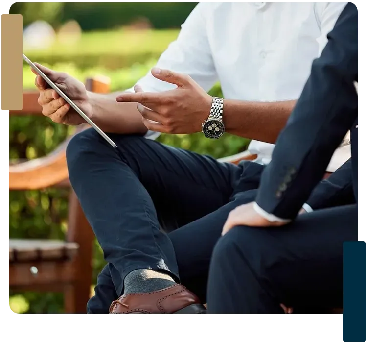 Two men are sitting on a bench looking at a tablet