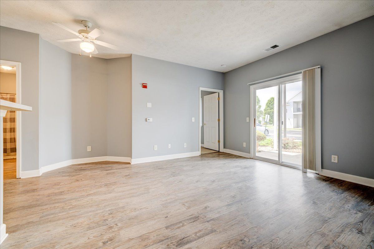 An empty living room with a ceiling fan and sliding glass doors.
