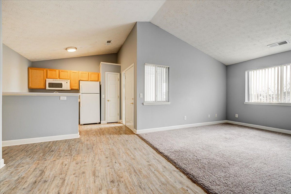 An empty living room with a rug and a kitchen in the background.