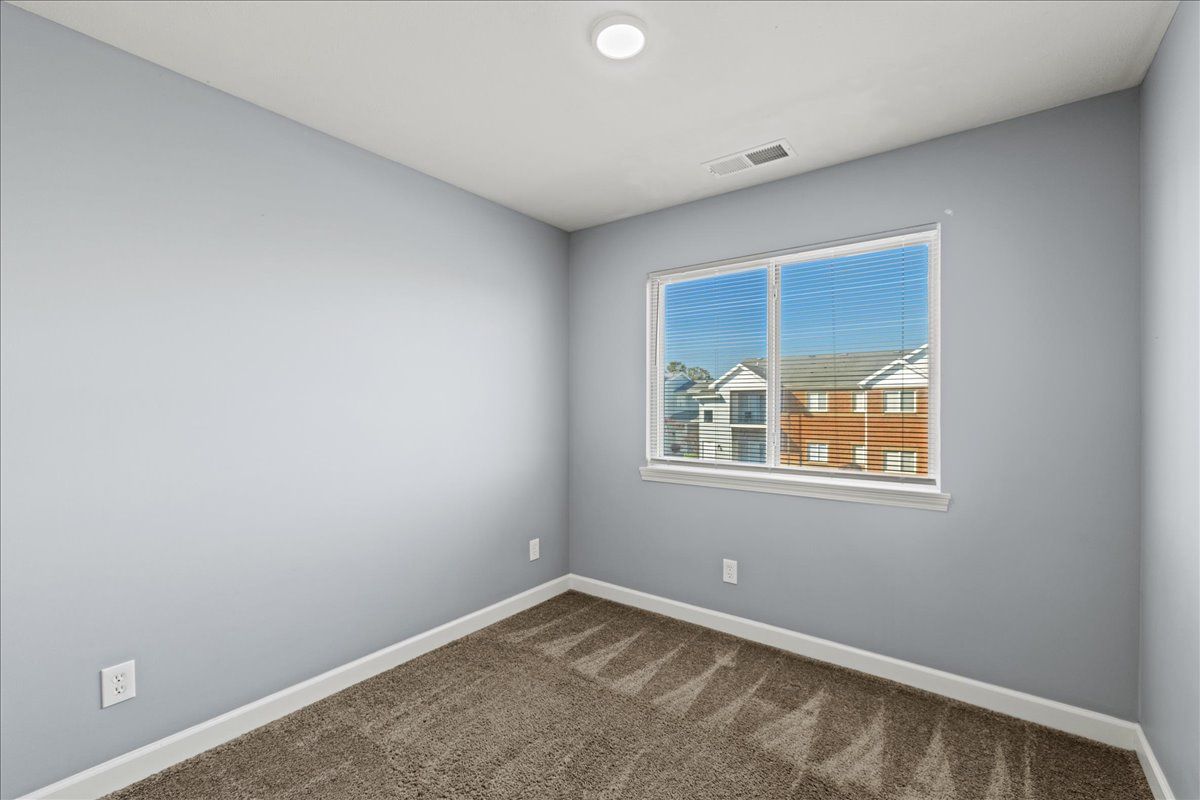 An empty bedroom with a window and a carpeted floor.