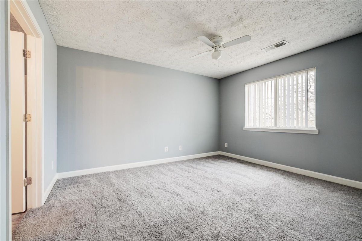 An empty bedroom with a ceiling fan and a window.