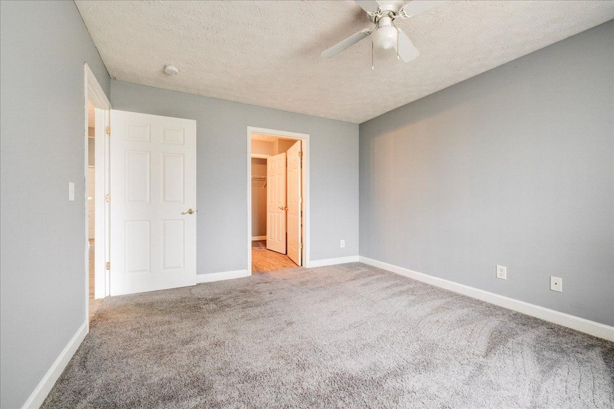 An empty bedroom with a ceiling fan and a gray carpet.