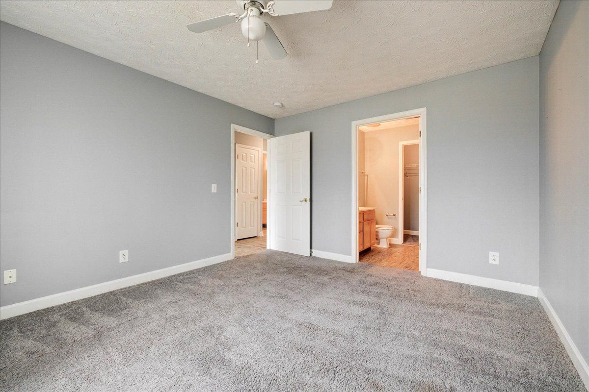 An empty bedroom with a ceiling fan and a gray carpet.