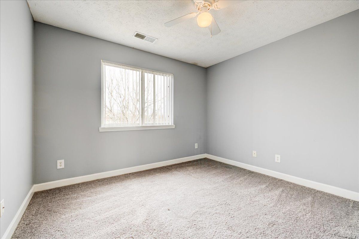 An empty bedroom with a ceiling fan and a window.