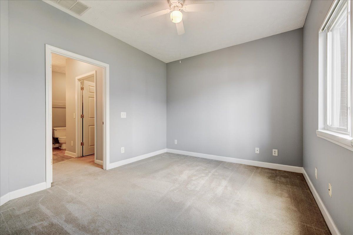 An empty bedroom with a ceiling fan and a window.
