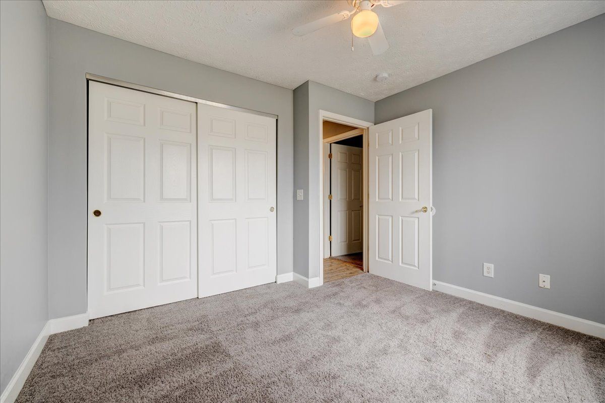 An empty bedroom with a ceiling fan and sliding doors.