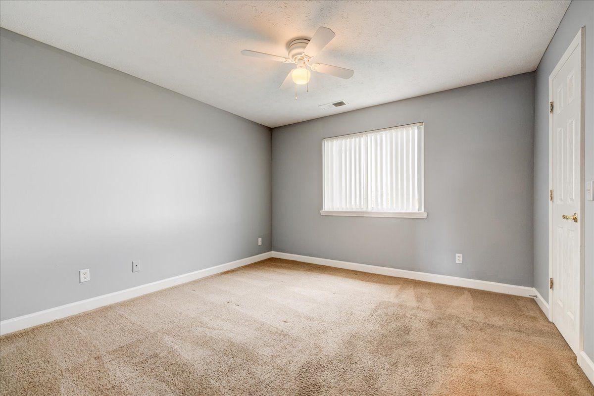 An empty bedroom with a ceiling fan and a window.
