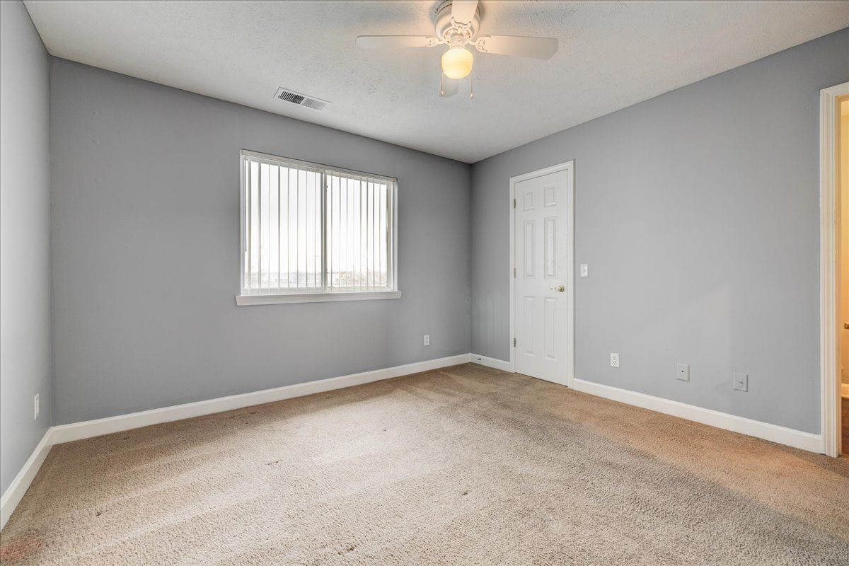 An empty bedroom with a ceiling fan and a window.