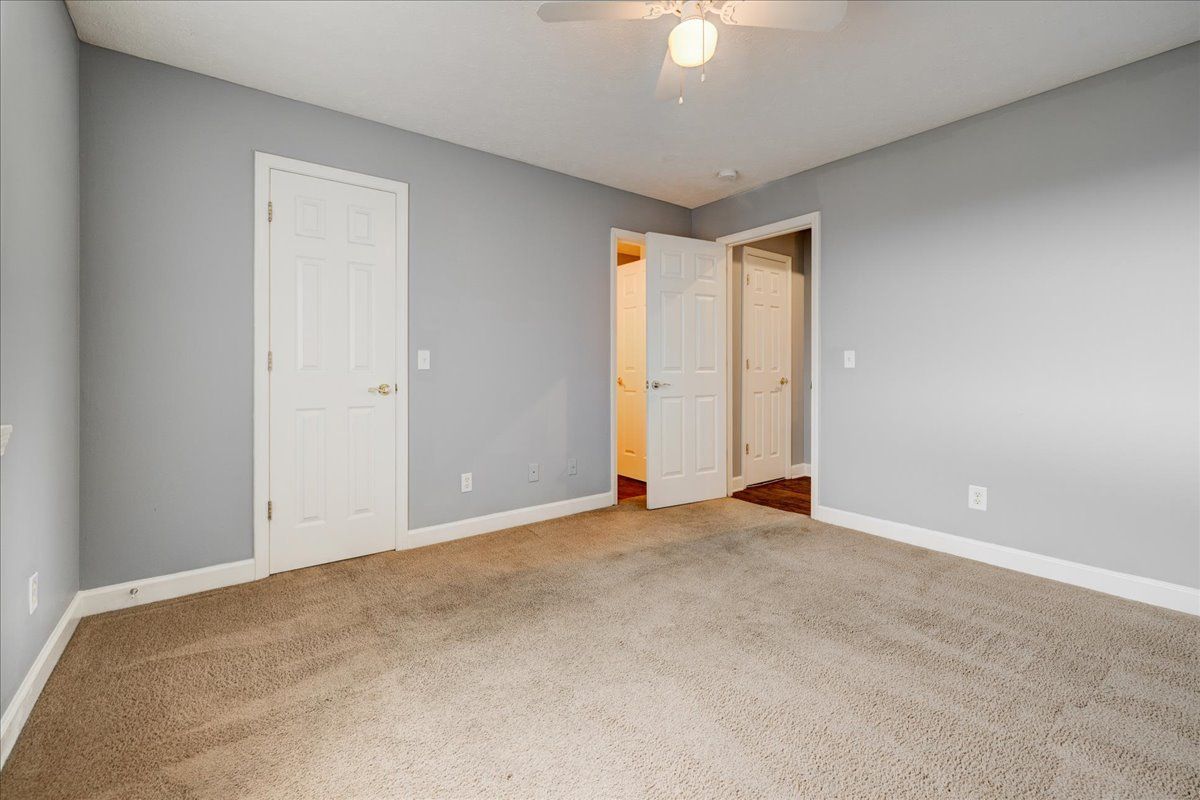 An empty bedroom with a ceiling fan and a carpeted floor.