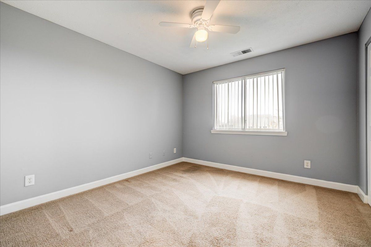 An empty bedroom with a ceiling fan and a window.