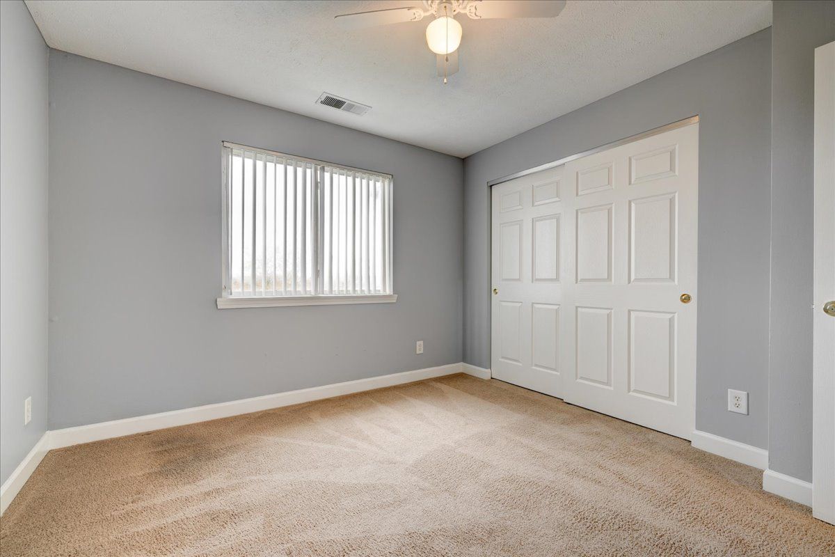 An empty bedroom with a ceiling fan and a window.
