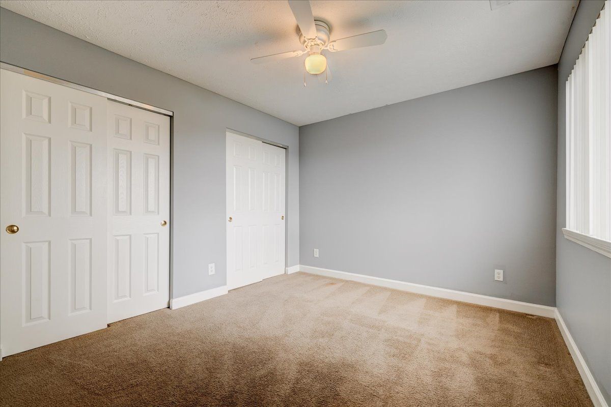 An empty bedroom with a ceiling fan and two closets.