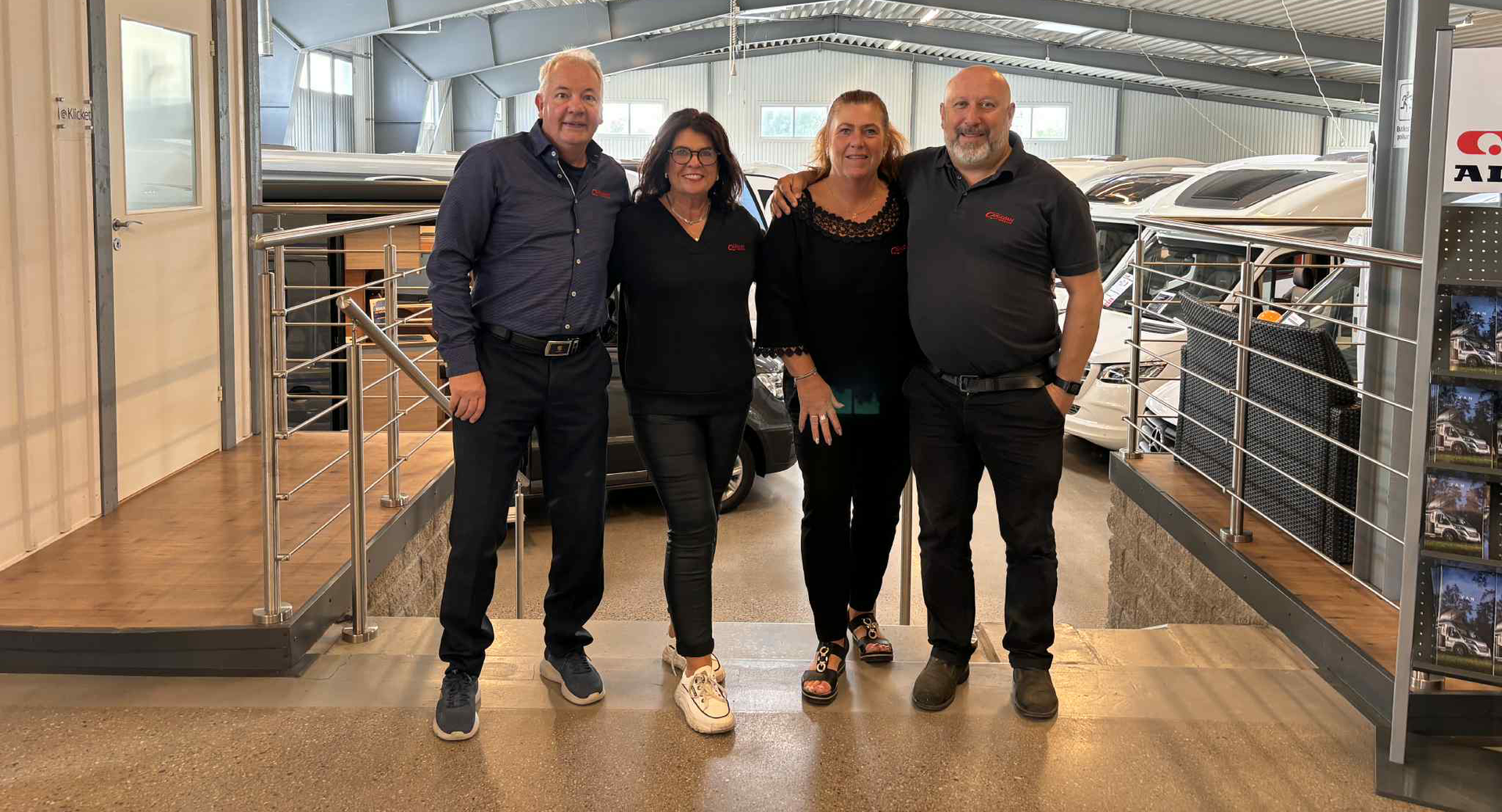 Five people standing inside a large warehouse.  They are smiling, some with arms around each other.  Marketing materials are visible.